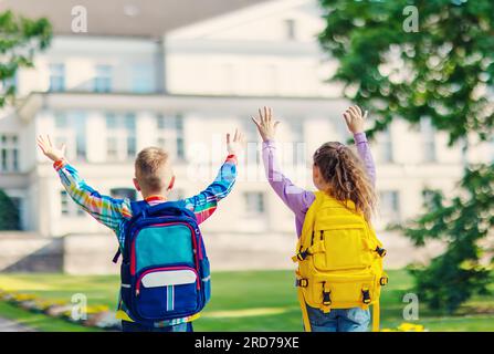 Girl and boy standing with raising hands in the park near the school. Stock Photo