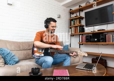 Young man music teacher giving guitar lessons to students online on laptop computer from home. Learning to play electric guitar using online course an Stock Photo
