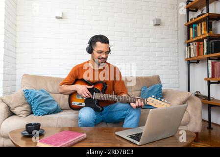 Young man music teacher giving guitar lessons to students online on laptop computer from home. Learning to play electric guitar using online course an Stock Photo