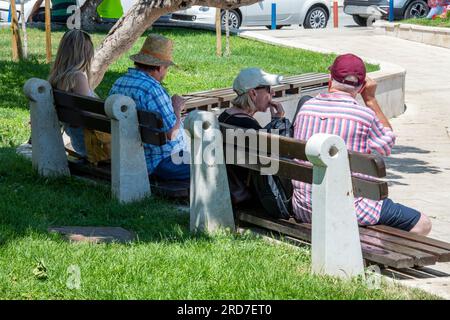 four people relaxing on a bench in the midday mediterranean sun in the city of split, croatia. men and women sitting on bench in park in high summer. Stock Photo