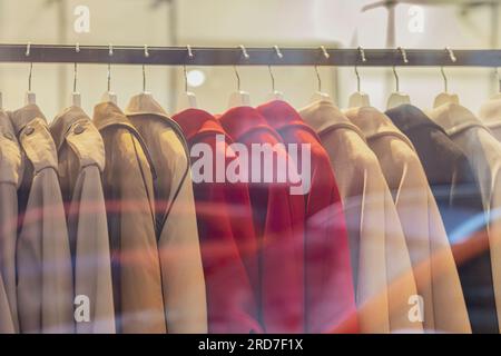 Colorful coats on hangers, assortment in clothing store. Autumn season sale. Blurred View through shop window, light bokeh, soft focus Stock Photo