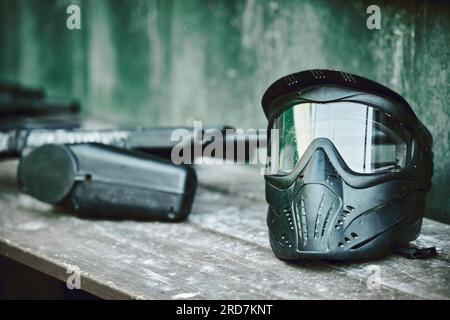 Paintball, helmet and gun on table at battle station of sports gear waiting for player, competition or war. Paint balling sportswear or stationary Stock Photo