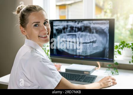 smiling dentist working with dental x-ray image on computer in clinics office Stock Photo