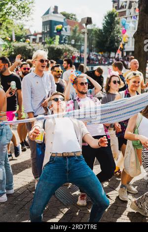 Amsterdam, North Holland, Netherlands – August 6, 2022: A young man in the middle of crowd celebrating Pride Amsterdam parade does impromptu limbo dan Stock Photo