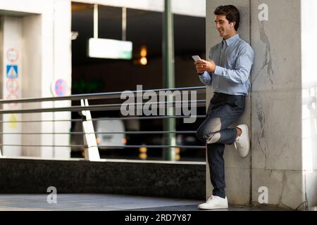 Young guy software engineer using smartphone and earbuds Stock Photo