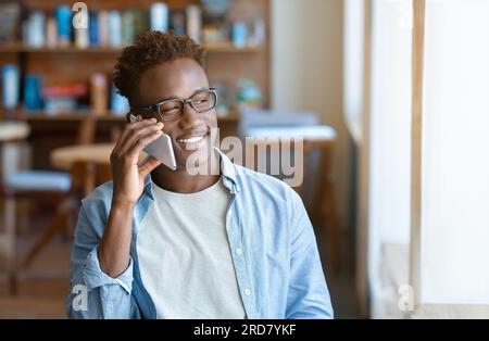 Happy black student speaking on mobile phone at urban cafe Stock Photo