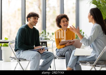 Happy diverse college students working together on study project in university classroom, sitting on chairs in circle Stock Photo