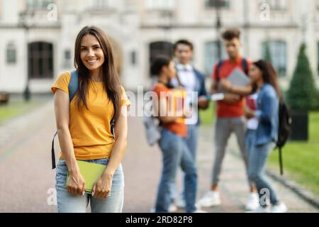 Student Life. Smiling young female posing in front college friends at campus Stock Photo