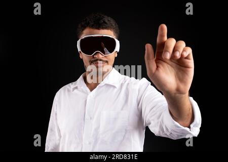 Young businessman using new vision pro VR glasses headset, gesturing and touching virtual screen over black background Stock Photo