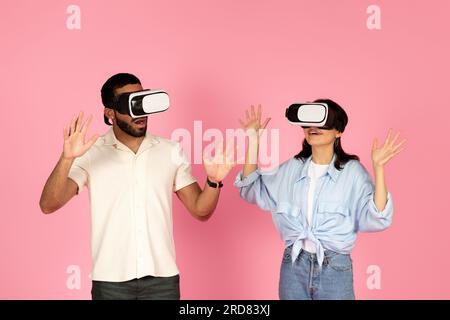 Surprised millennial guy and woman using VR glasses, pink background Stock Photo