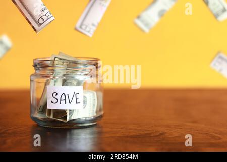 Save money for the future. Glass jar with dollars on a wooden table. Piggy bank with banknotes and dollars flying around. copy space. The concept of f Stock Photo