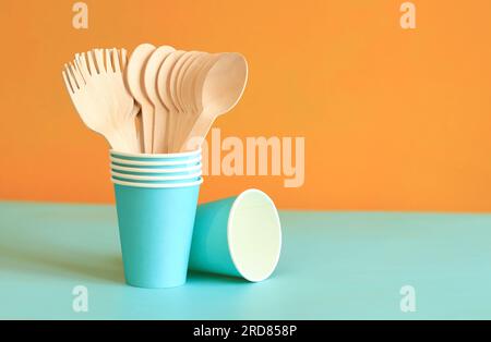 Wooden disposable forks and spoons in a blue paper cup, side view. Eco friendly disposable kitchen utensils on orange background, copy space. Ecologic Stock Photo