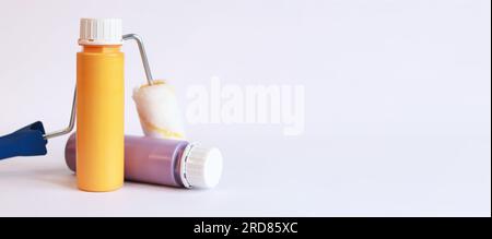 Two bottles of acrylic paint and a paint roller on a light background, side view. Paints for repair and redesign Stock Photo