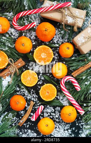 Christmas background with tangerines, candies, gifts and fir branches on a dark table with fake snow, top view. Stock Photo