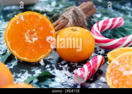 Christmas composition, cut tangerine, cinnamon tubes and candy cane against the background of fir branches Stock Photo