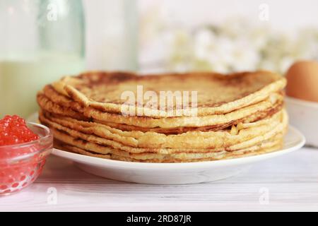 Stack of freshly baked pancakes lie in white plate. Pancake week. Selective focus. Glass bottle with milk, crepes, caviar and egg Stock Photo