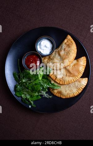 top view fried chebureks with sauce and herbs on a black plate. Stock Photo