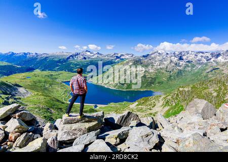 One man looking at the alpine lake of Montespluga standing on rocks, Madesimo, Valle Spluga, Valtellina, Lombardy, Italy, Europe Stock Photo