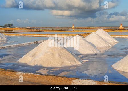 Piles of salts among salt flats with windmills in the background at sunset, Saline Ettore e Infersa, Marsala, province of Trapani Stock Photo