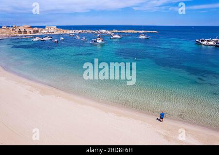 Aerial view of tourist standing in an empty white sand beach looking at the sea in front of the fishing village of Marzamemi Stock Photo