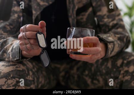Unhappy man in camouflage uniform sitting at arm chair over white studio background, touching his head, soldier suffering from posttraumatic stress Stock Photo