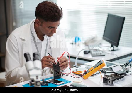 Repairman using multimeter to check if smartphone battery works Stock Photo