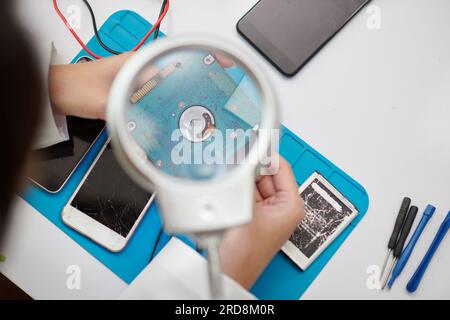 Technician looking through magnifying glass when examining computer hard drive Stock Photo