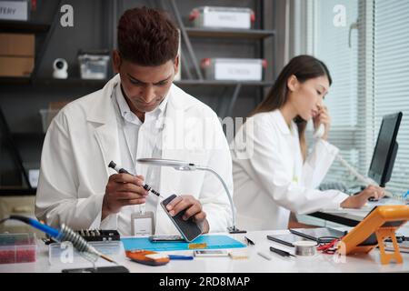 Technician reassembling smartphone when manager talking on phone with client Stock Photo