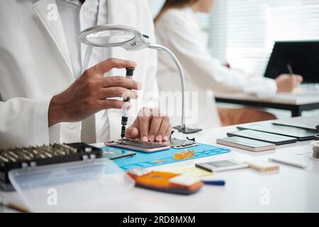 Technician looking through magnifying glass when reassembling broken smartphone Stock Photo