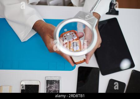 Technician using magnifying glass when examining broken feature phone Stock Photo