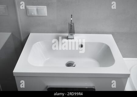 Modern bathroom interior, white washbasin with drawers, chrome faucet, socket and switch on the wall. Bathroom interior with sink and faucet. Stock Photo