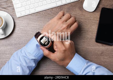 Businessman checking home security system via smartwatch app at office table, top view. Image of room through CCTV camera on display Stock Photo