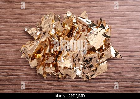 Many pieces of edible gold leaf on wooden table, top view Stock Photo