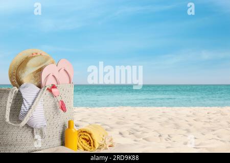 Bag with bikini and accessories on sunny ocean beach, space for text. Summer vacation Stock Photo