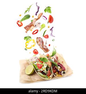 Delicious tacos. Ingredients falling into tortillas on white background Stock Photo