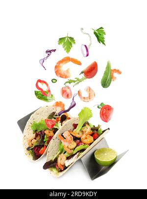 Delicious tacos. Ingredients falling into tortillas on white background Stock Photo