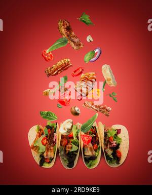 Delicious tacos. Ingredients falling into tortillas on red background Stock Photo