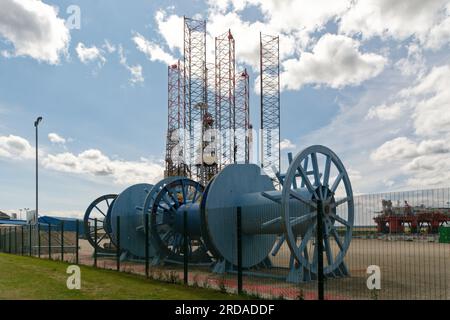 Large Blue Cable Reels in the foreground of an oil rig construction area in Invergordon, Scotland. Jack Up Rig legs in the background. Stock Photo