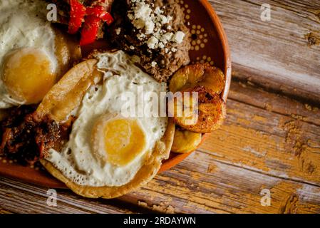 Huevos rancheros, meat, beans, and fried plantains in a clay dish. Typical Mexican food. Stock Photo