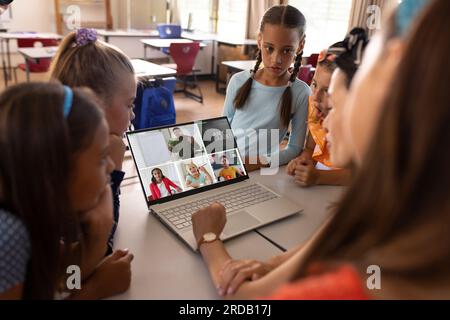 Diverse teacher and students video calling over laptop while studying online in classroom Stock Photo