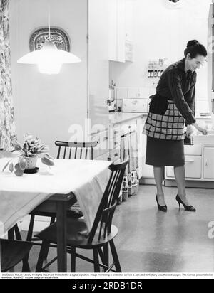 In the kitchen 1960s. Interior of a kitchen and a women taking something from a kitchen drawer. Sweden 1960 Stock Photo