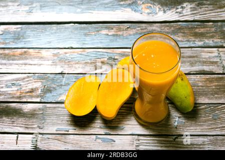 Glass of mango juice and sliced mangoes on wooden table. Colorful scene. Stock Photo