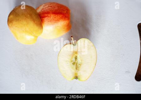 Sliced bisected raw Gala apples on white cutting board, top view. Half an red and yellow riped apple for cooking in domestic kitchen. Halved juicy swe Stock Photo