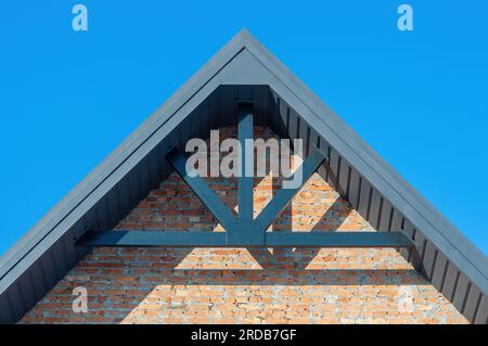 The gable of the house is made of brick and the roof with hemmed soffits, the construction of the roof with decorative beams Stock Photo