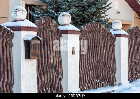 Original fence made of wooden boards and stone pillars with balls. The fence of the homestead, with a mailbox Stock Photo