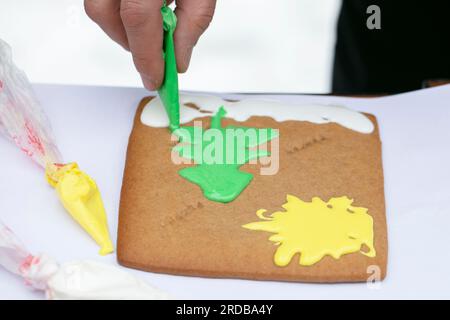 Hand draws Christmas tree on gingerbread with cream icing. Stock Photo