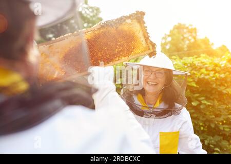 Happy female beekeeper and man holding honeycomb frame in garden Stock Photo