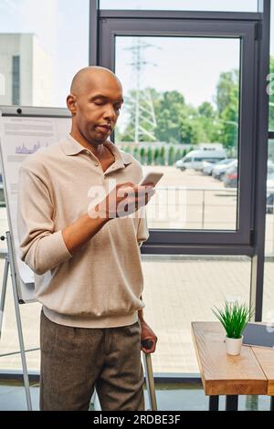 myasthenia gravis, bold african american businessman with eye syndrome using smartphone and standing with walking cane, dark skinned office worker wit Stock Photo