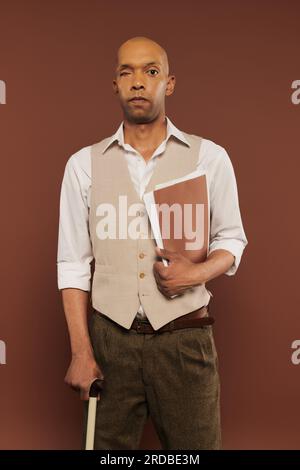 inclusion, bold african american man with myasthenia gravis syndrome, standing with walking cane and holding folder, dark skinned man with chronic dis Stock Photo