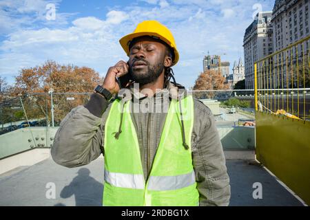 young black man boss manager worker of construction company standing outdoors with closed eyes is upset and tired talking on the phone, communication Stock Photo